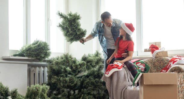 glückliche eltern mit tochter stellen ihren weihnachtsbaum im wohnzimmer zu hause auf - christmas tree christmas tree artificial stock-fotos und bilder