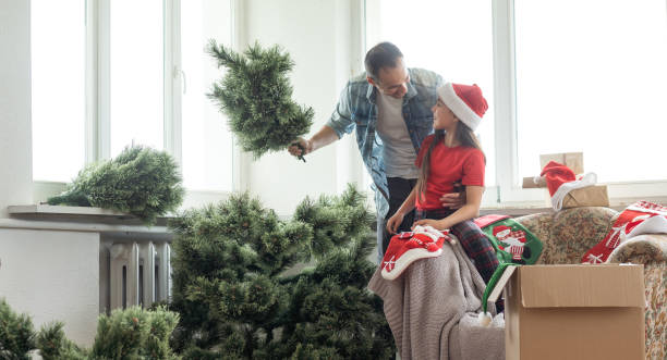 genitore felice con figlia impostare il loro albero di natale nel soggiorno di casa - christmas tree christmas tree artificial foto e immagini stock