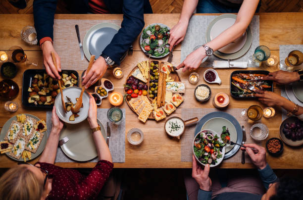 Unrecognizable Friends And Family Sharing Food At Dinning Room From above photo of group of friends enjoys eating delicious vegetarian food during a dinner celebration. dining table stock pictures, royalty-free photos & images