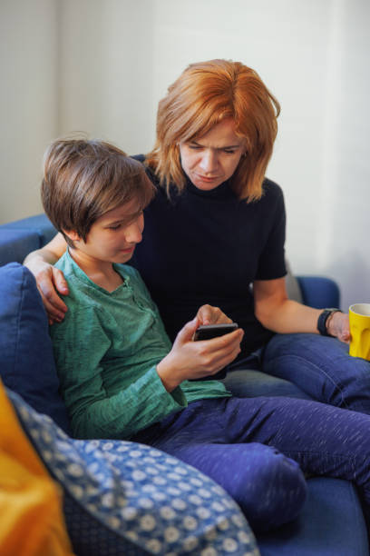 istock Boy holding smart phone and watching content with his mother on the sofa 1427535300