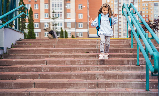 Back to elementary, primary school. Little sad girl with big backpack goes in hurry, late to first grade alone in autumn morning. Education, future of children. Happy,unhappy pupil kid on stair steps.