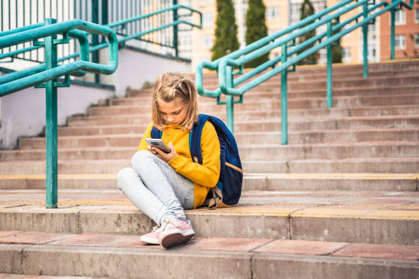 istock Back to elementary, primary school. Little girl with backpack,mobile phone. Chat, talk with friends, classmates on break. Autumn study after vacation. Education of children. Pupil kid on stair steps 1427539864