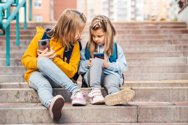 istock Back to elementary,primary school. Little girls with backpack,mobile phone.Chat, talk with mom,friends, classmates on break.Autumn study after vacation. Education of children.Pupil kid on stair steps 1427539868
