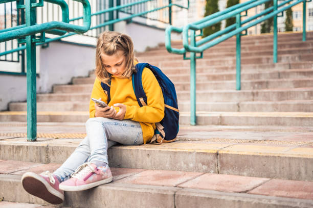 istock Back to elementary, primary school. Little girl with backpack,mobile phone. Chat, talk with friends, classmates on break. Autumn study after vacation. Education of children. Pupil kid on stair steps 1427539869