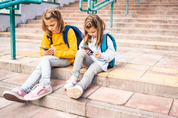 istock Back to elementary,primary school. Little girls with backpack,mobile phone.Chat, talk with mom,friends, classmates on break.Autumn study after vacation. Education of children.Pupil kid on stair steps 1427539894