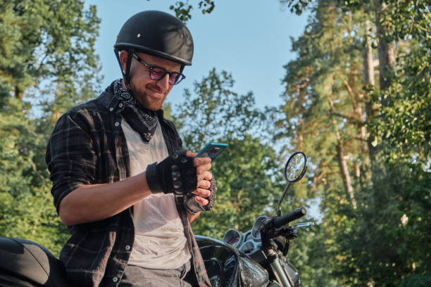 istock Young male biker in helmet using mobile phone and smiling sitting on a motorcycle 1427540628