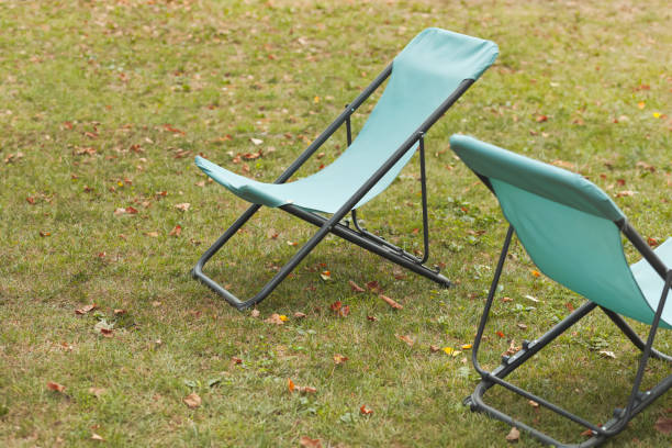 istock Light blue foldable canvas chairs empty on grass with fallen leaves, close up 1427542493