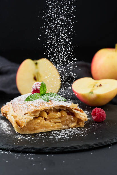 Baked strudel with apples sprinkled with powdered sugar on a black board Baked strudel with apples sprinkled with powdered sugar on a black board, delicious dessert sprinkling powdered sugar stock pictures, royalty-free photos & images