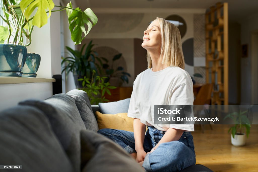 Happy adult woman sitting on the sofa with eyes closed enjoying bright daylight Women Stock Photo