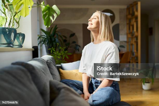 Happy Adult Woman Sitting On The Sofa With Eyes Closed Enjoying Bright Daylight Stock Photo - Download Image Now