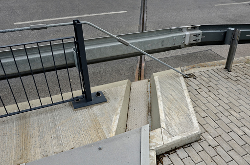 the space between the lanes of the highway bridge is blocked by a grid. the guardrails are in combination with the black metal railing bolted to the concrete bridge, tension rod, expandable, dilatation