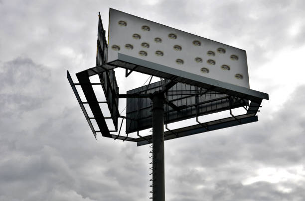 A large billboard sign on blue sky is empty, made of heavy steel and double sided in Los Angeles business section downtown surrounded by street lights, telephone poles, and traffic signal and wires on a mostly clear day symbolizes the recession's power to steal money from advertising