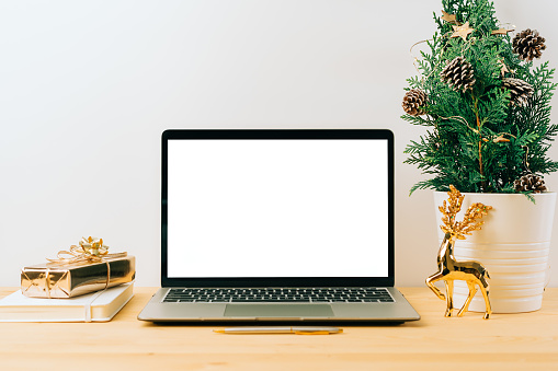 Laptop with mockup blank screen on wooden table with Christmas gift, fir tree on white background. Computer with Mock up and copy space for text.
