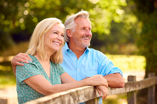 Smiling Casually Dressed Mature Or Senior Couple Leaning On Fence On Walk In Countryside