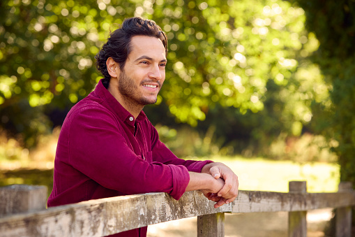 Smiling Casually Dressed Mature Man Leaning On Fence On Walk In Countryside