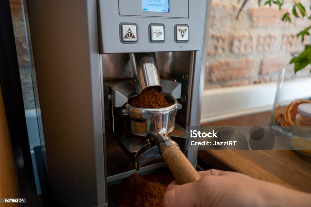 Freshly ground coffee pouring into portafilter in espresso machine Brewery Stock Photo