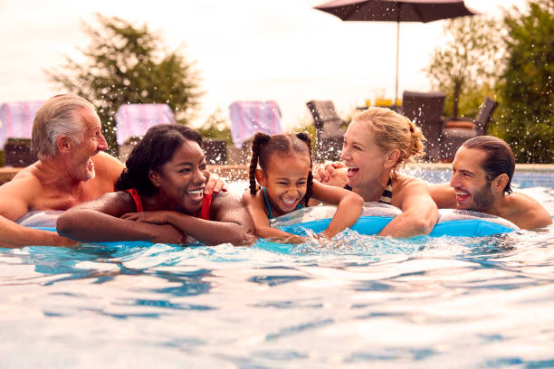 família multigeragração sorridente nas férias de verão relaxando na piscina no airbed - swimming swimming pool senior adult child - fotografias e filmes do acervo