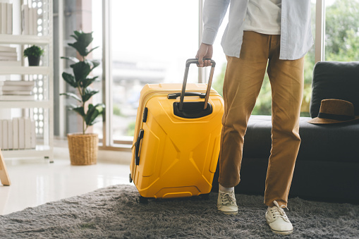People getting ready for holidays travel trip concept. Single traveller man walking carry a luggage begin a journey. Men wear casual cloth and sneakers. Background in living room at home or hotel.