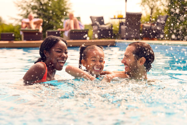 Smiling Mixed Race Family On Summer Holiday Having Fun Splashing In Outdoor Swimming Pool stock photo