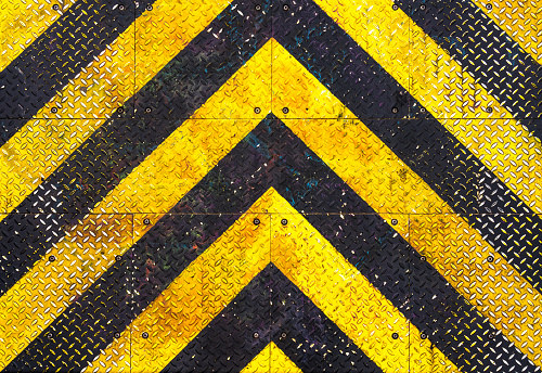 A heavily worn background of industrial steel, painted with a black and yellow chevron pattern.