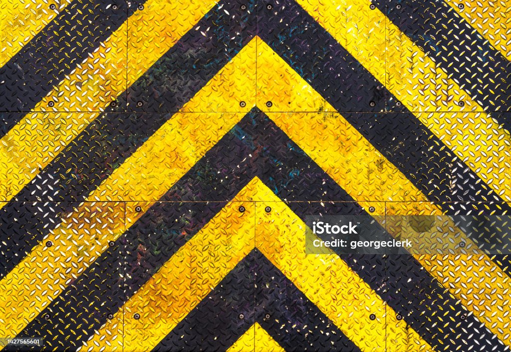 Weathered industrial chevron pattern on diamond plate steel background A heavily worn background of industrial steel, painted with a black and yellow chevron pattern. Warning Sign Stock Photo