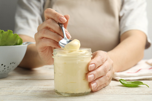 Woman with jar of delicious mayonnaise at white wooden table, closeup