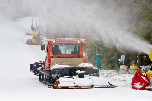 Tucker County, West Virginia, USA - January 18, 2022: A snowcat grooms a slope at Blackwater Falls State Park as a snow-making cannon blasts new “snow” onto the hill.