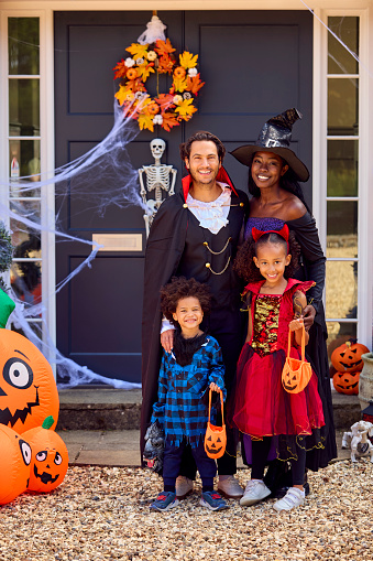 Portrait Of Family Dressed Up For Halloween Outside House Ready For Trick Or Treating