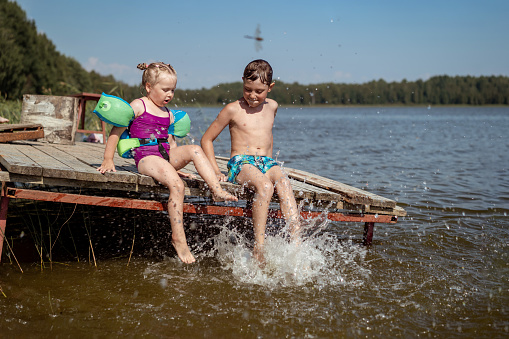 cute children splashing watter sitting on wooden pier by lake in countryside. High quality photo