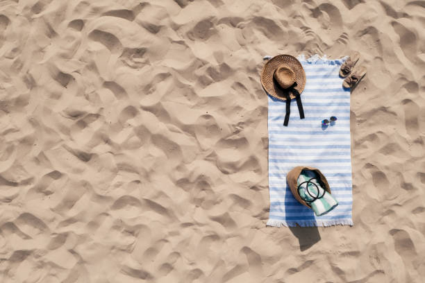 Towel with beach accessories on sand, top view. Space for text