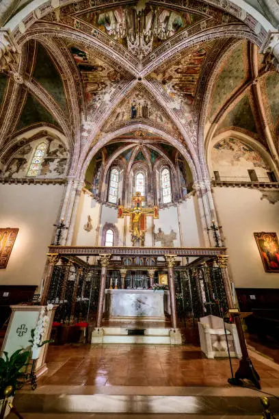 The presbytery and the main altar inside the Basilica di Santa Chiara (Saint Clare Basilica), in the medieval heart of Assisi, in Umbria. Built in the Gothic style between 1257 and 1265, this basilica preserves in its crypt the mortal remains of Santa Chiara and is the seat of the Order of the Poor Ladies or Order of Saint Clare. In the photo, the hanging crucifix is the work of the Master of Santa Chiara, an artist of the late thirteenth century, while the frescoes in the vault are attributed to the Expressionist Master of Santa Chiara, an artist instead a follower of Giotto, datable to around 1337. An ancient Umbrian city built starting from the 9th century BC, Assisi became in 89 BC an important center of social and economic domination of Ancient Rome. After the fall of Rome and countless looting due to the barbarian invasions, in the Middle Ages Assisi was conquered by the Byzantines and the Lombards, finally ending up under the dominion of the emperor Frederick I the Barbarossa. Assisi, famous for being the city of Saint Francis and Saint Clare, is a sacred and spiritual place, a world symbol of peace between all the peoples of the earth and the different confessions. The Umbria region, considered the green lung of Italy for its wooded mountains, is characterized by a perfect integration between nature and the presence of man, in a context of environmental sustainability and healthy life. In addition to its immense artistic and historical heritage, Umbria is famous for its food and wine production and for the quality of the olive oil produced in these lands. Since 2000 the Basilica and other Franciscan sites of Assisi have been declared a World Heritage Site by UNESCO. Image in high definition format.