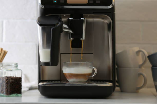 istock Modern espresso machine pouring coffee into glass cup with milk on white countertop in kitchen 1427570141