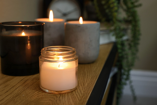 Lit candles in different holders on wooden table indoors. Space for text