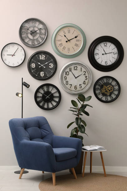 istock Armchair, table and many different clocks hanging on white wall in room 1427573487