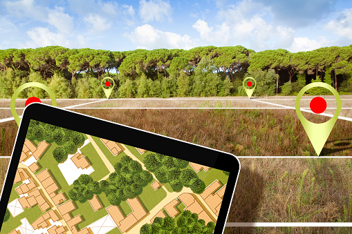 Real estate concept with a vacant land and cadastral parcel available for building construction  near a forest with digital tablet and imaginary cadastral map and city planning