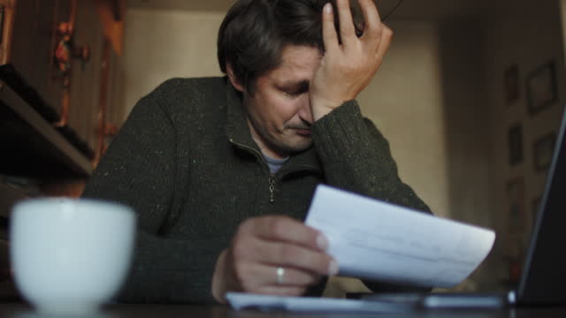 Worried man checking bills, frustrated about high prices and having financial problems
