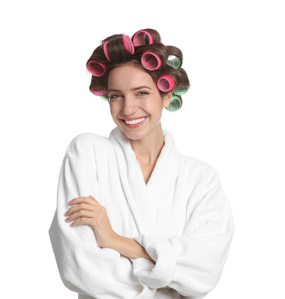 Beautiful young woman in bathrobe with hair curlers on white background