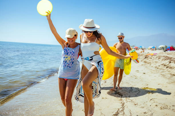 Below view of young woman throwing Frisbee to group of her friends on the beach.