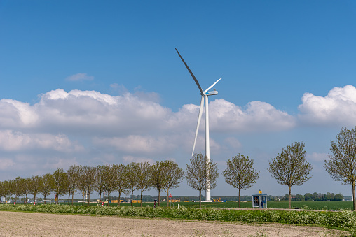 Lelystad, Netherlands - May 07,2022: Windmill, row of trees, polder and road