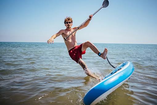 Man falling off stand up paddle board into the sea