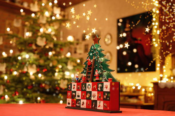 Three-dimensional Advent Calendar with stylised Christmas Tree in the middle of Christmassy illuminated Family Room painted advent calendar made of wood with stylised Christmas Tree, tiny figures and drawers standing on a table in the middle of a Christmassy decorated and illuminated family room advent calendar stock pictures, royalty-free photos & images