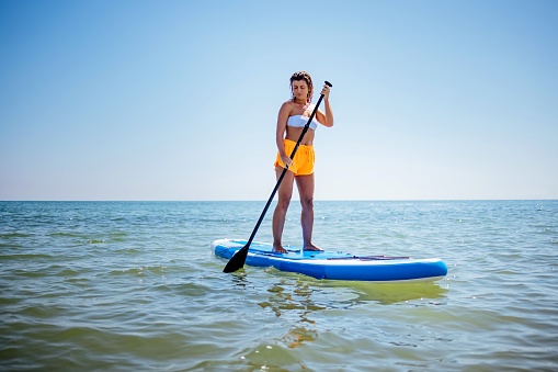 Woman paddles her stand up paddle board through the waves
