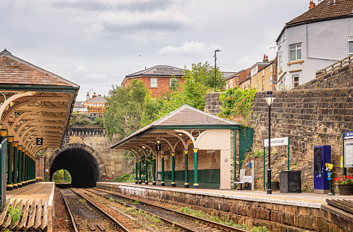 Knaresborough, UK. September 20, 2022.  Two railway station canopies supported by green columns are aside the entrance to a tunnel. Rails lead into the tunnel and the a sky with cloud is above.