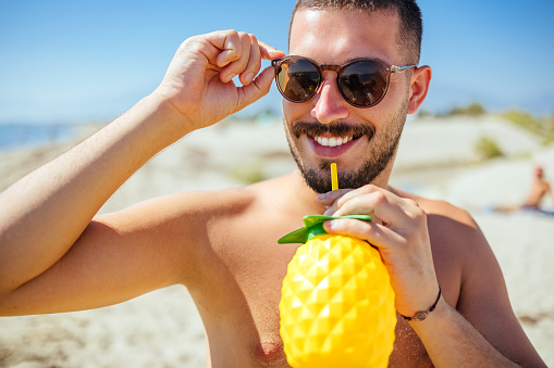 Young man drinking cocktail on sandy beach