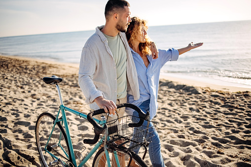 Loving couple sits by the sea and pushes a bicycle