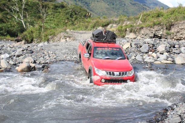インドネシア、トリカラ - 2018年3月30日:トリカラ地区パプアの岩だらけの川を渡る赤いストラーダトリトン4x4車 - triton designer label ストックフォトと画像