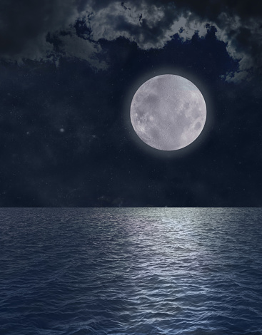 Dark blue night scene with moonlit clouds and reflection on water surface of sea, ocean or lake ideal for a spiritual spooky or halloween concept
