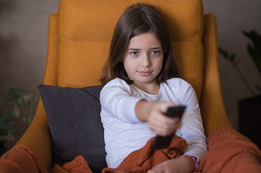 Young girl sitting comfortably on the sofa and holding a remote controller