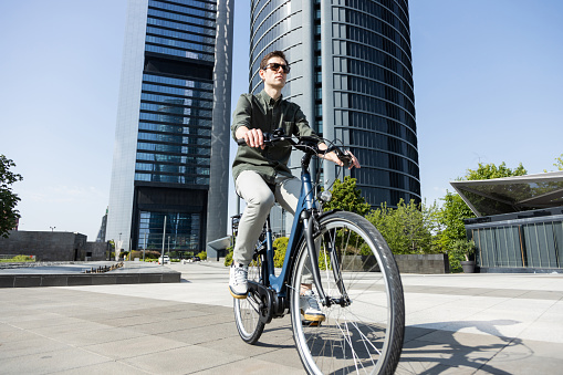 young businessman rides e-bike on his way to the tower where his office is located