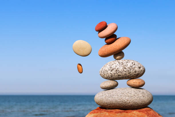 The fall of the pyramid of balanced stones on blue sky background. The concept of fall risk and unstable equilibrium. The fall of the pyramid of balanced stones on blue sky background. The concept of fall risk and unstable equilibrium unbalance stock pictures, royalty-free photos & images